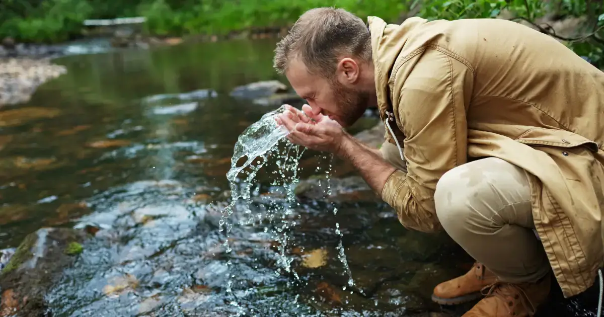 barbat care se spala pe fata cu apa din rau