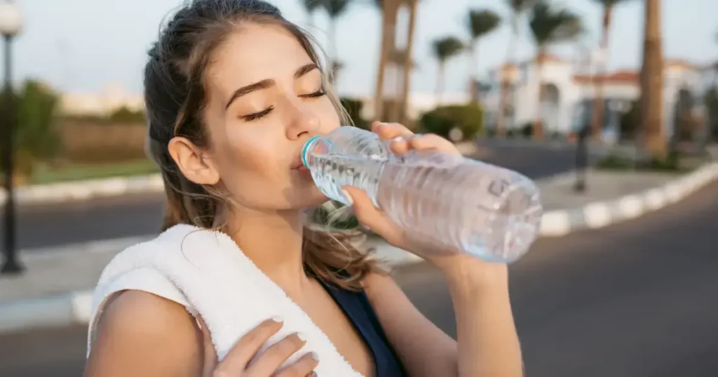 fata care bea apa dintr-o sticla de plastic