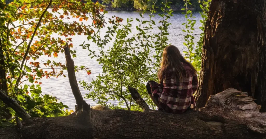 Fata care sta singura in natura pe marginea apei