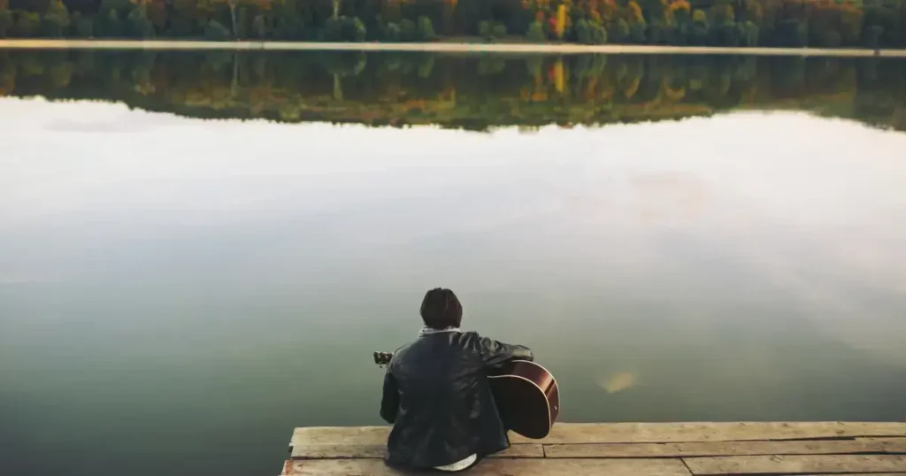 Tanar cu chitara care sta pe un doc, la marginea lacului